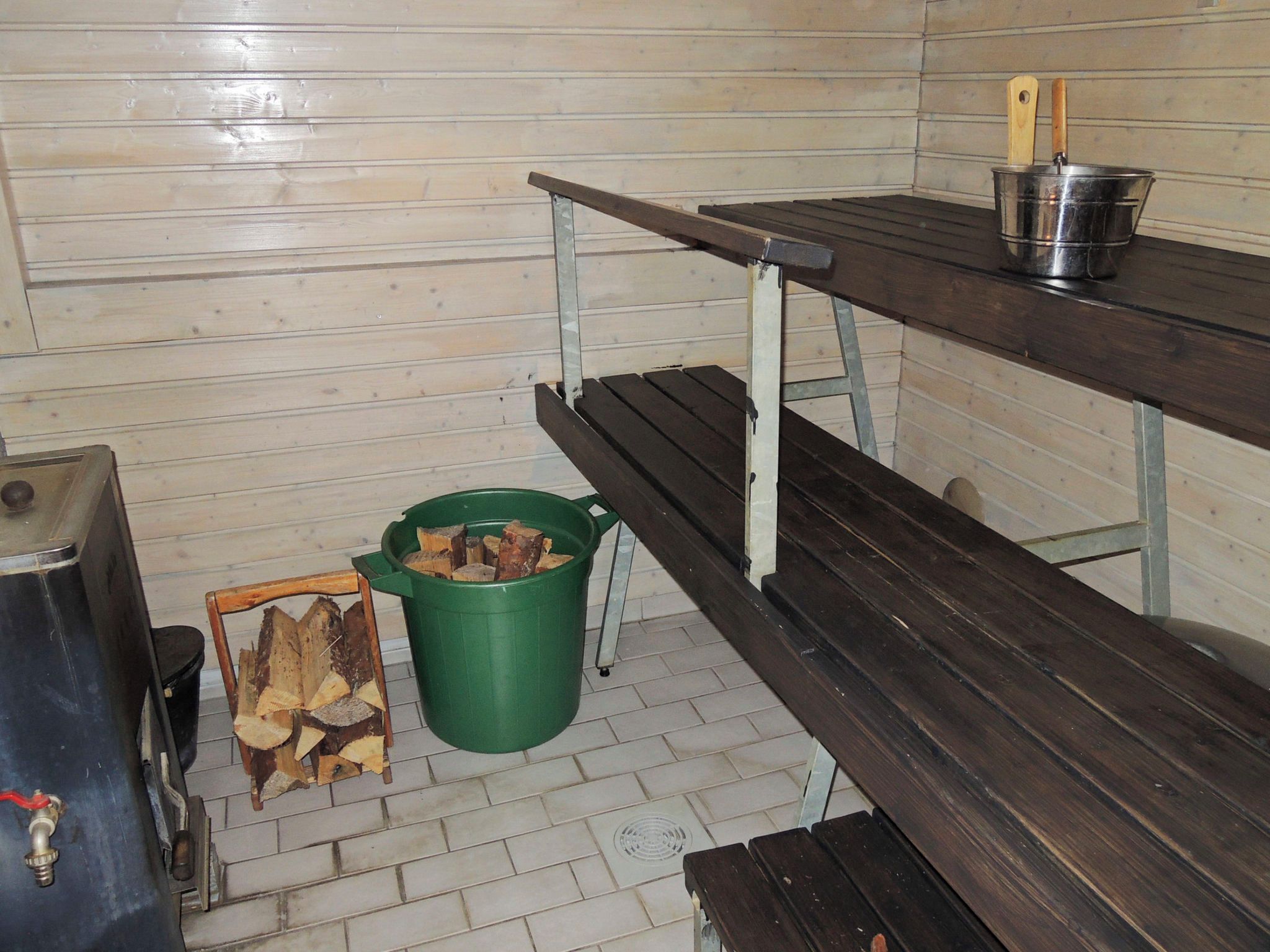 A wooden bench with a metal frame, a green bucket with firewood, and a metal pot on a table.