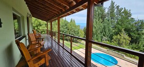 A wooden deck with chairs overlooking a swimming pool and a lush green landscape. - Buena Vida Social Club (El Bolson)
