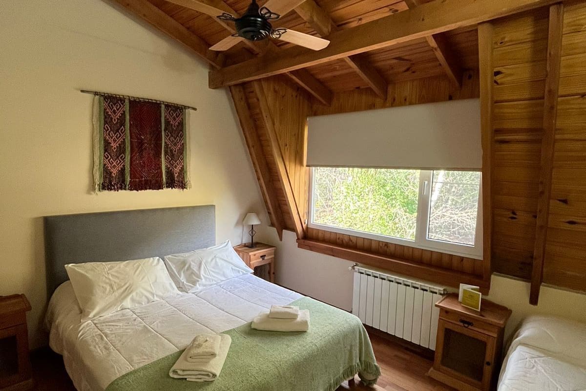 A wooden cabin bedroom with a bed, a window, a radiator, and a ceiling fan.