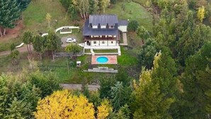 A large two-story house surrounded by dense forest, with a swimming pool and a well-maintained lawn. - Buena Vida Social Club (El Bolson)