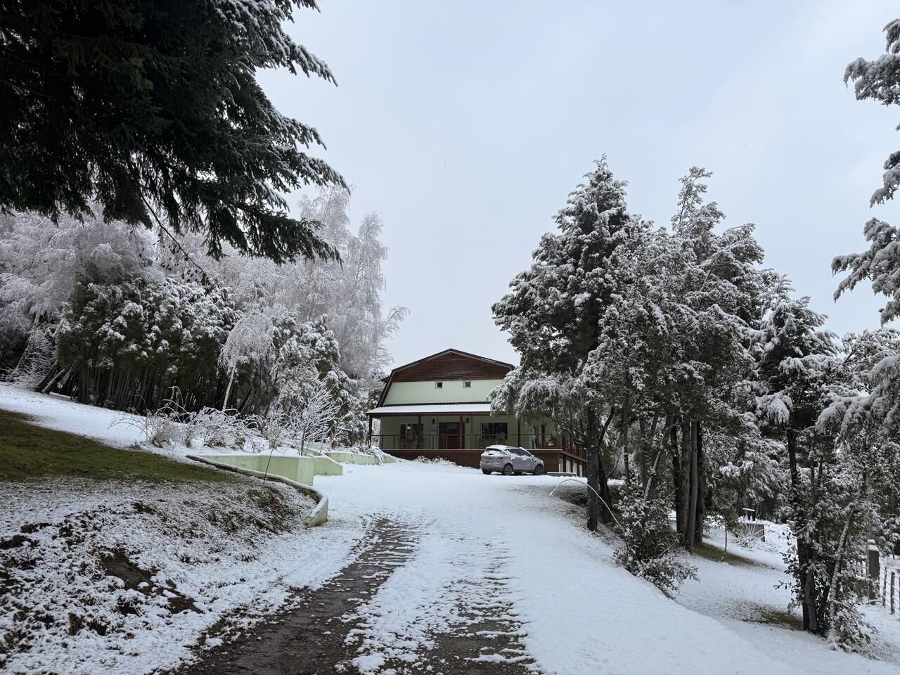 A snow-covered pathway leading to a building with a red roof and a white exterior.