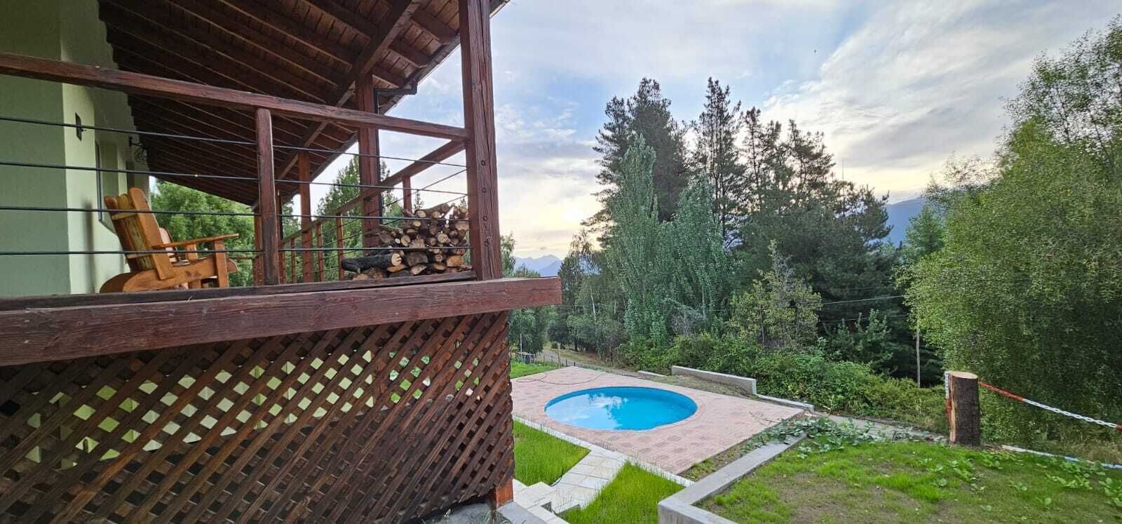A wooden balcony with a chair, a stack of firewood, and a swimming pool in the background.