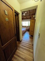 A hallway with wooden flooring leading to a bedroom with a bed and a window.