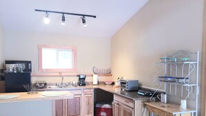 A compact kitchen with wooden cabinets, a built-in oven, a coffee maker, and a metal rack with glass containers. - “Cozy Mountain Suites - #5 just 5 minutes from Glacier Park (Coram)