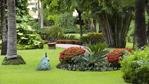 Un jardin luxuriant agrémenté d’un paon, de palmiers et de diverses plantes à fleurs.
