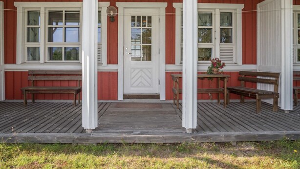 Un edificio rosso con decorazioni bianche, un portico in legno e tre panchine.