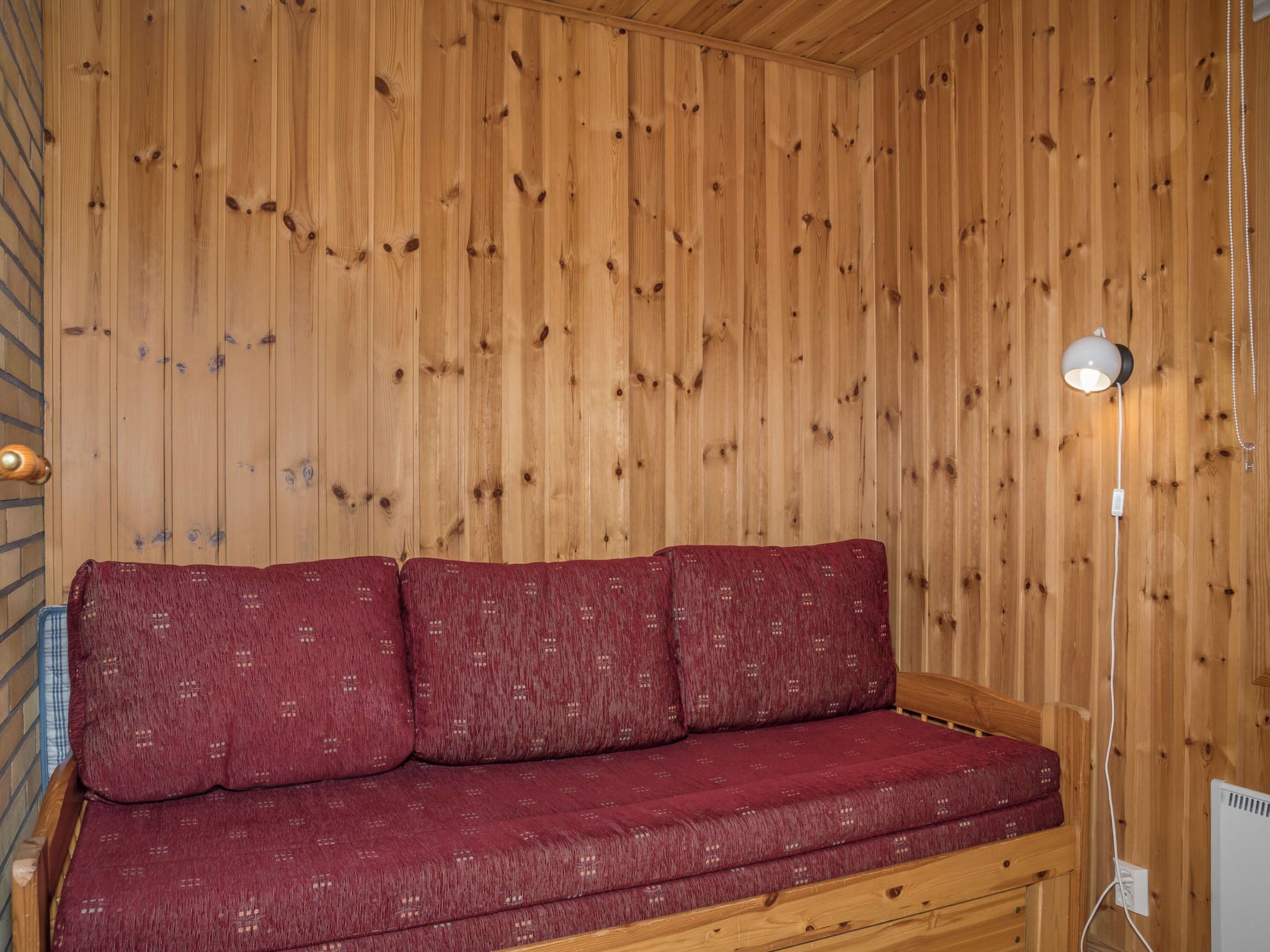 Een houten interieur met een rode bank tegen een houten wand, een lamp en een stopcontact.