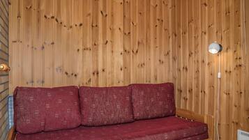 Een houten interieur met een rode bank tegen een houten wand, een lamp en een stopcontact.