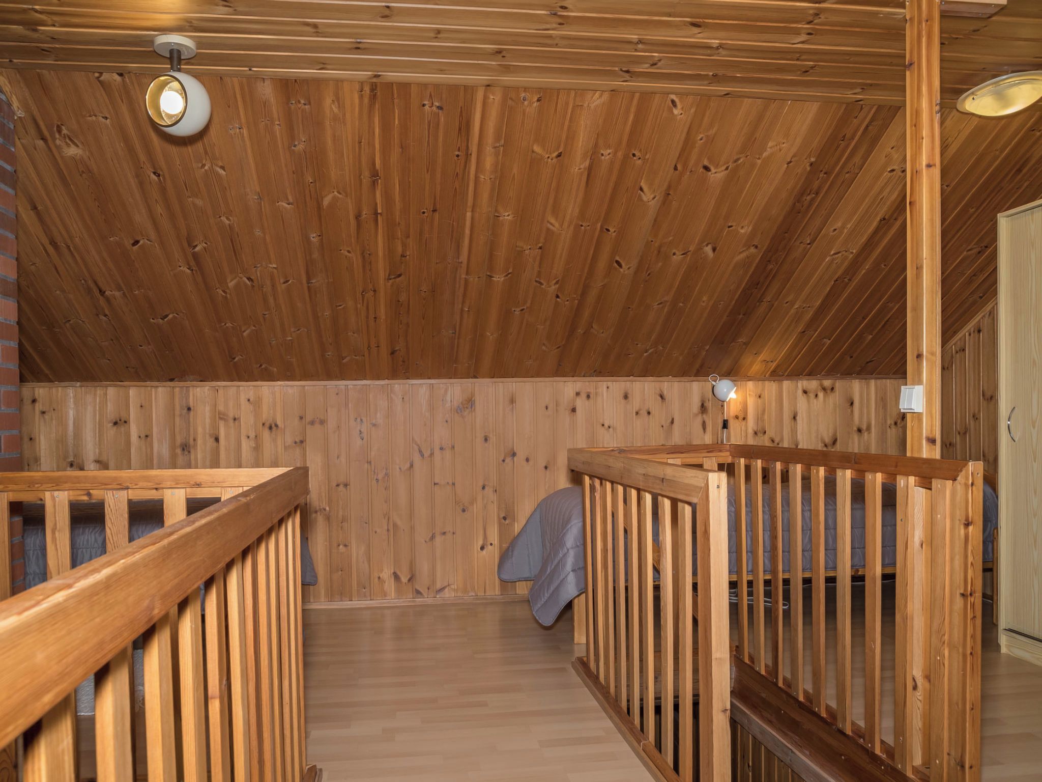 A wooden interior with a sloped ceiling, wooden railings, and a mattress on the floor.