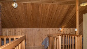 Una camera da letto mansardata con pareti in legno, un soffitto spiovente, un letto singolo e una piccola finestra.