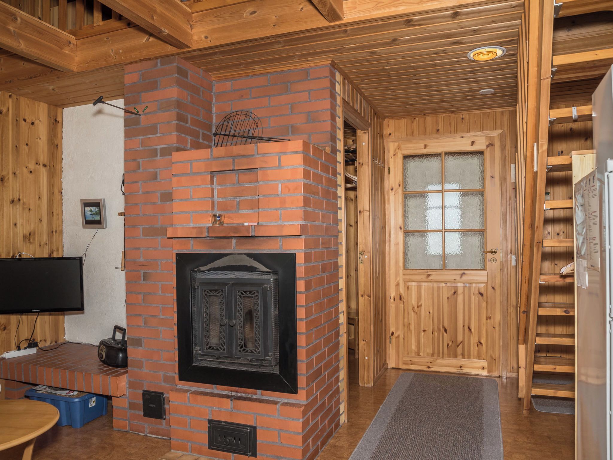 A cozy room with a brick fireplace, wooden walls, a television, and a door with frosted glass panels.
