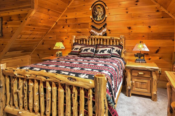 A log cabin bedroom with a wooden bed, a nightstand with a lamp, and a wall hanging.