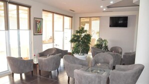 A modern interior with grey upholstered chairs, a glass coffee table, and a large potted plant. - Hotel Coral (Vlorë)