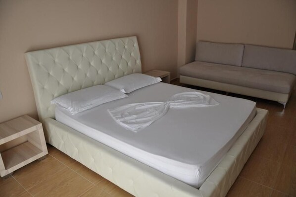 Una cama bien hecha con cabecera capitonada, una mesita de noche y un sofá en una habitación de hotel.