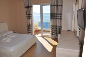 Habitación de hotel con cama, televisor, balcón con una silla y vista al mar.
