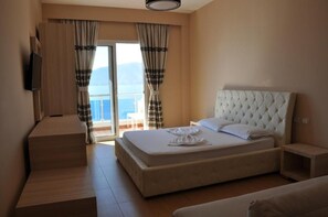 A hotel room with a bed, a TV, a balcony with curtains, and a view of the sea. - Hotel Coral (Vlorë)