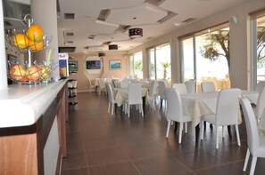 Un comedor con sillas y mesas blancas, una exhibición de frutas y un letrero con el nombre Bull.