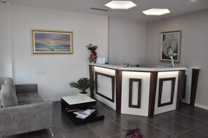 Un espace d’accueil doté d’un bureau moderne, d’un canapé gris et de deux œuvres d’art encadrées accrochées aux murs.