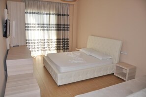 Un dormitorio con una cama, una mesita de noche, un televisor y una ventana con cortinas.
