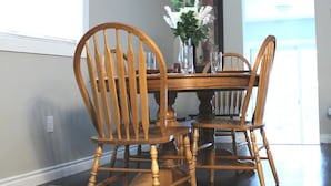 A dining area with a wooden table and chairs, a vase with flowers, and a window with natural light.