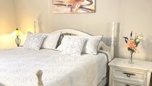 A neatly made bed with a white headboard, a bedside table with drawers, and a wall-mounted painting.