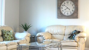 A living room with two beige sofas, a glass coffee table, and a large wall clock.