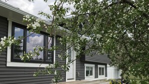A house with a wooden deck, large windows, and a garden with flowers.