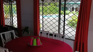 Une table recouverte d’une nappe rouge, quatre chaises blanches et un plateau avec trois tasses.