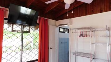 A room with a ceiling fan, a TV mounted on the wall, a door with a window, and a metal shelf unit.