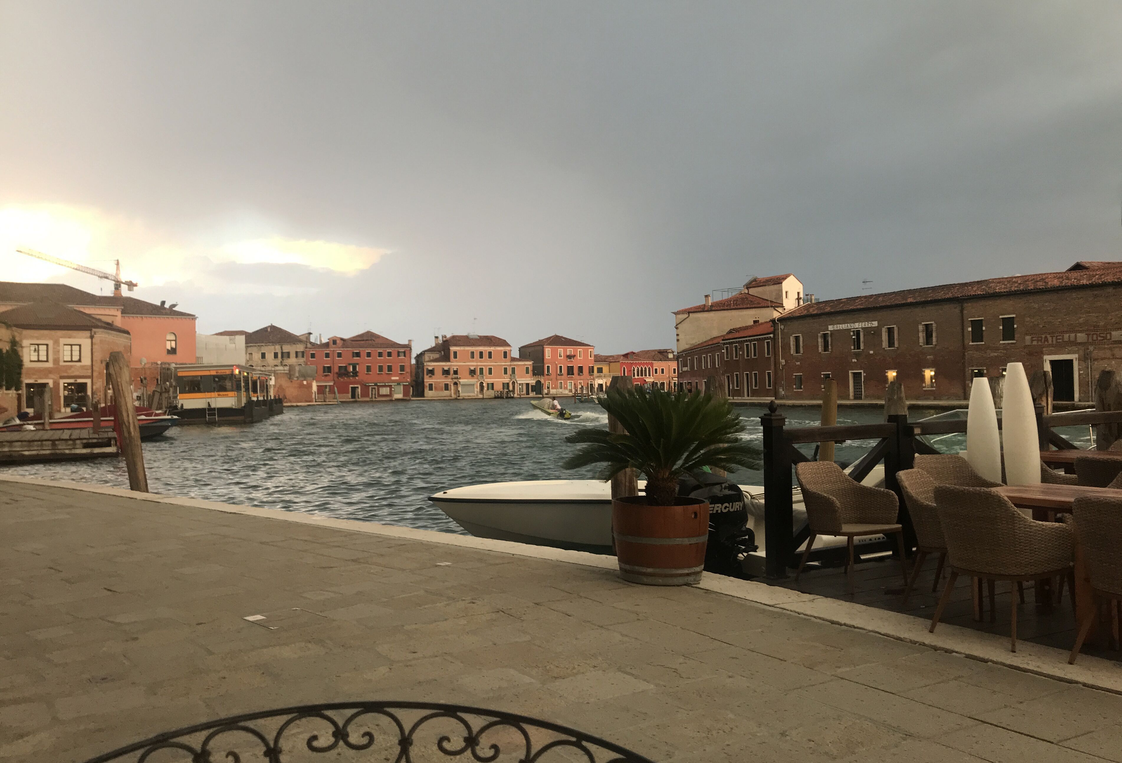 A waterfront view with buildings, a boat, and outdoor seating.