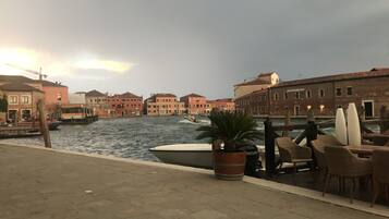 A waterfront view with buildings, a boat, and outdoor seating.