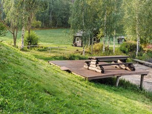 A picnic area with a wooden bench and a picnic table, surrounded by a grassy field and trees. - Savilahti by Interhome (Juuka)