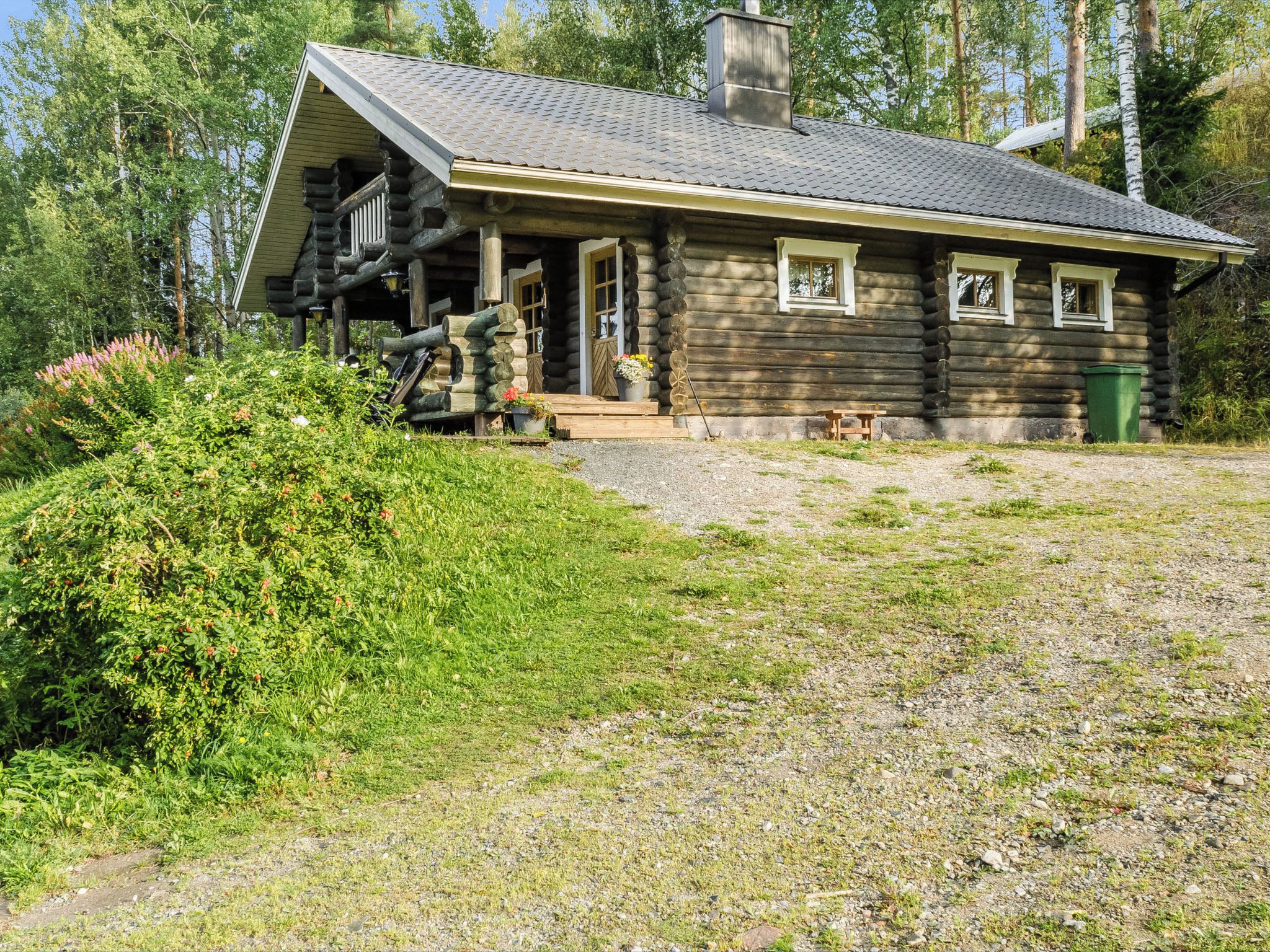 A log cabin with a porch, a chimney, and a gravel driveway.