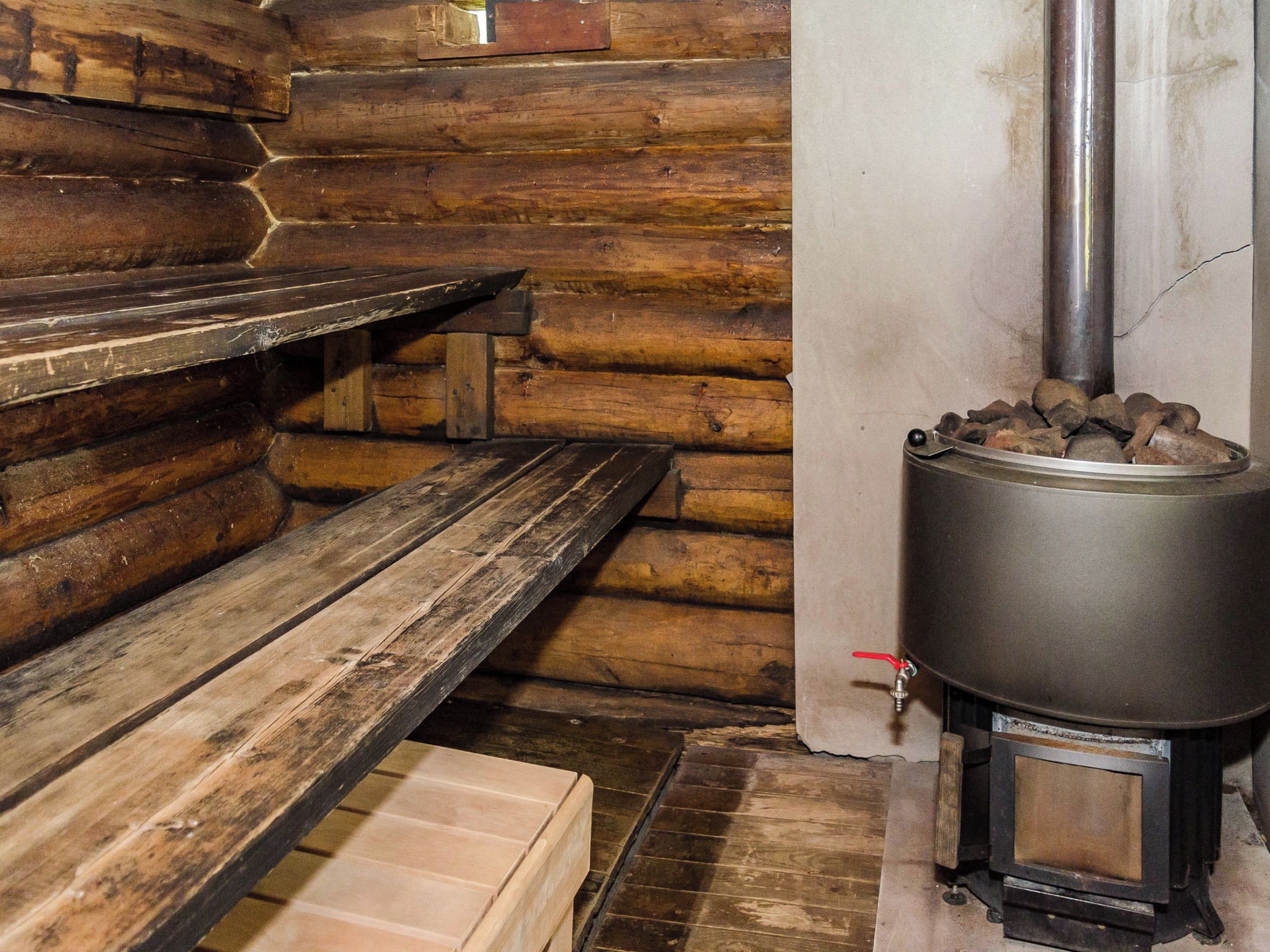 A log cabin interior with a wooden bench and a wood-burning stove.