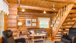 A cozy log cabin interior with a wooden staircase, a sofa, armchairs, and a dining table. - Savilahti by Interhome (Juuka)