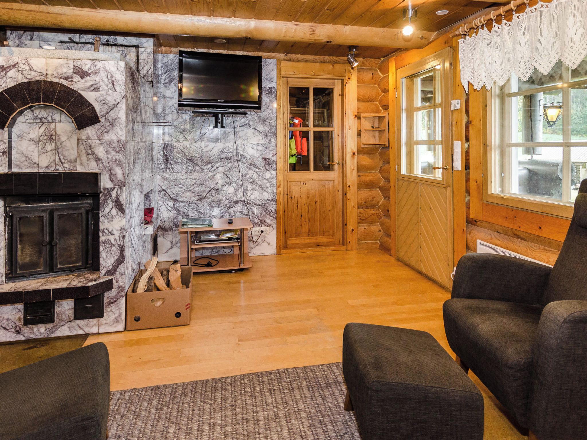L’intérieur d’une cabane en rondins est agrémenté d’une cheminée, d’un téléviseur fixé au mur et d’un coin salon confortable avec deux fauteuils.