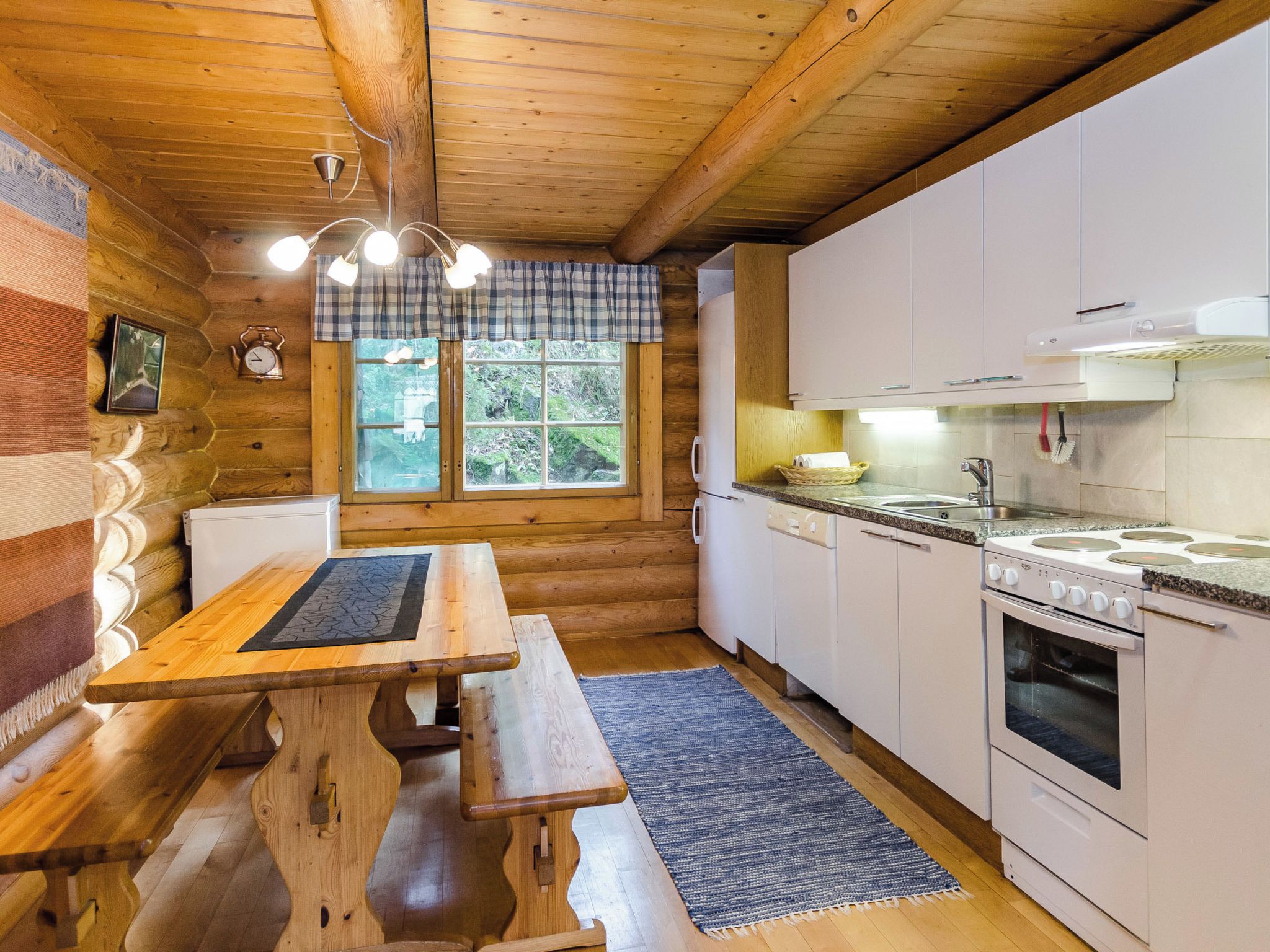 A wooden cabin interior with a kitchen, dining table, and bench.