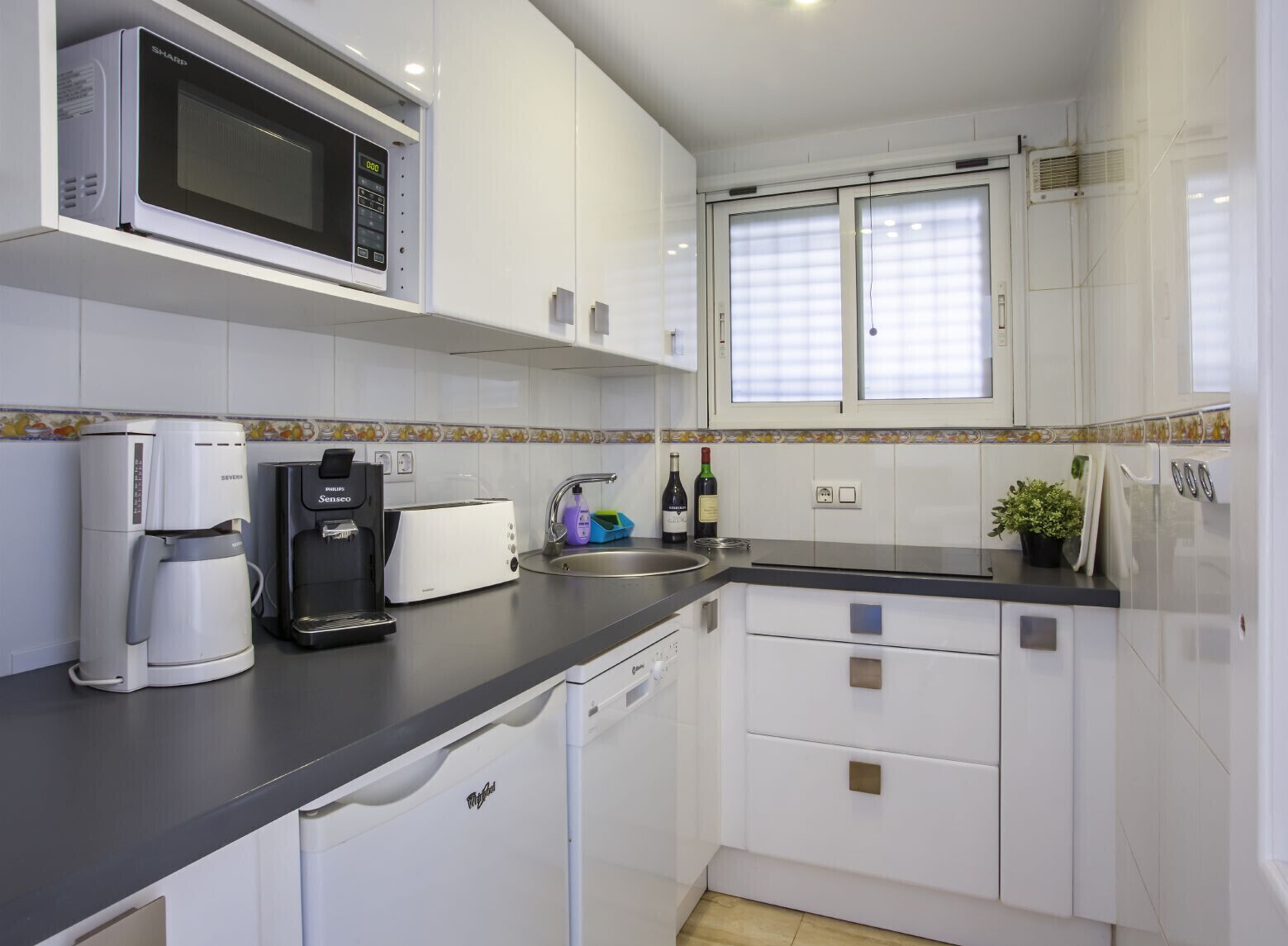 A modern kitchen with white cabinets, a microwave, a coffee maker, a toaster, and a sink.