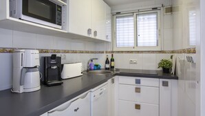Une cuisine moderne avec des meubles blancs, un four à micro-ondes, une machine à café, un grille-pain et un évier.