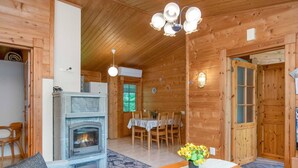 A cozy cabin interior with a fireplace, wooden walls, a dining area, and a living room with a sofa and a table with flowers. - Rusakko by Interhome (Sotkamo)