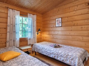 A cabin room with two beds, a window with curtains, a wall-mounted lamp, and a framed picture. - Rusakko by Interhome (Sotkamo)