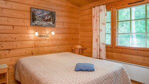 A cozy wooden cabin room with a bed, a small table, a chair, and a window with curtains. - Rusakko by Interhome (Sotkamo)