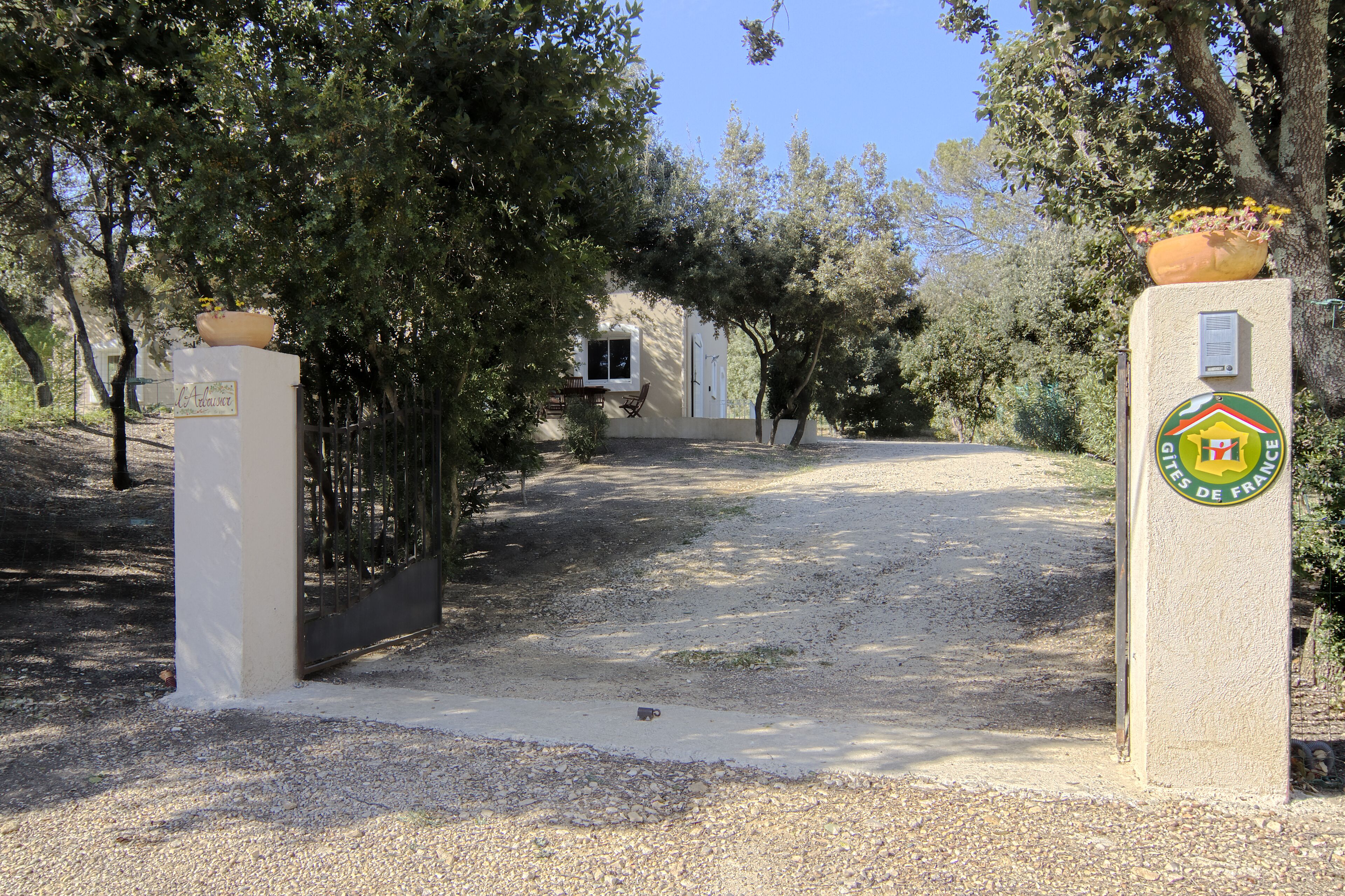Une allée de gravier mène à un bâtiment doté d’une porte et d’une fenêtre, le tout étant entouré d’arbres.