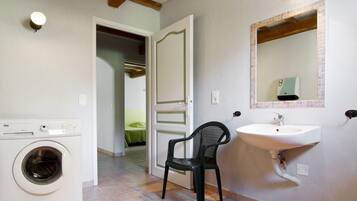 A bathroom with a washing machine, a sink, and a chair.