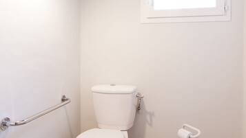 Ein kleines, sauberes Badezimmer mit Toilette, Handläufe, Fenster und Toilettenpapierhalter.