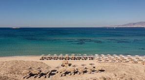 A beach with sun loungers and thatched umbrellas, clear blue water, and distant mountains. - Golden Sand Naxos (Naxos)