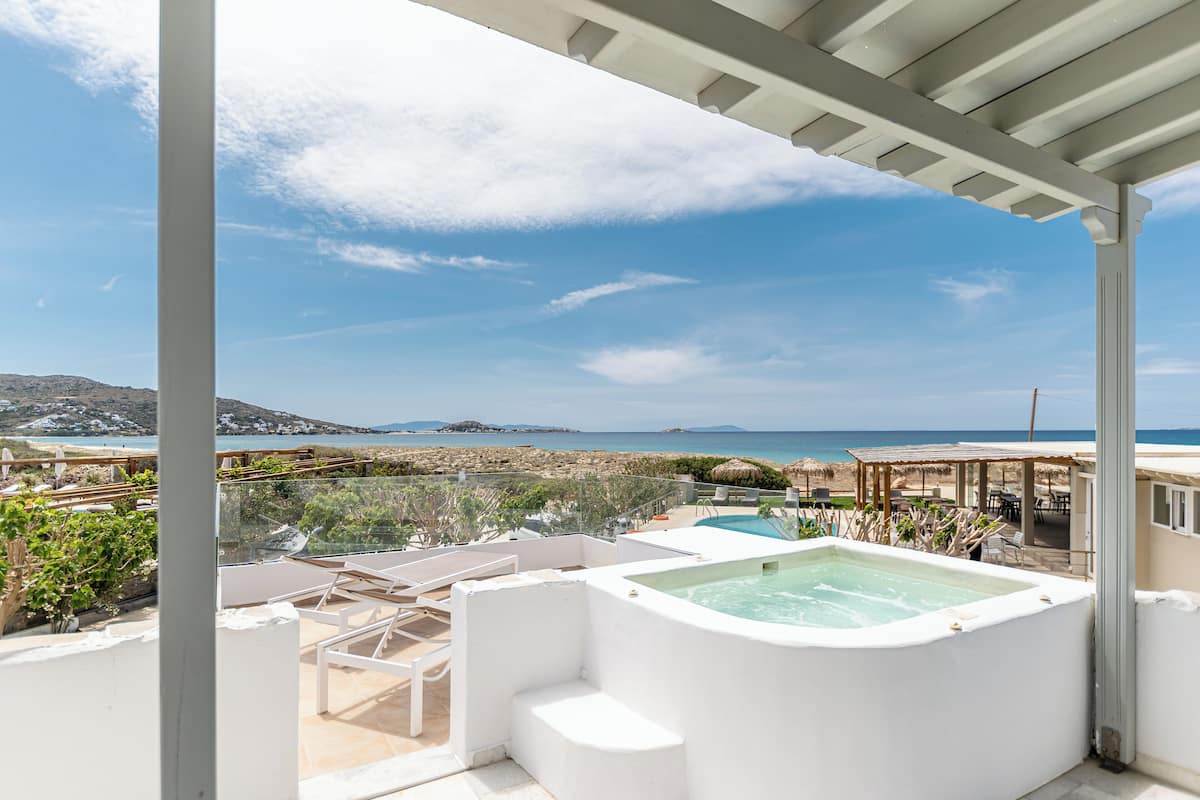 A rooftop terrace with a hot tub, lounge chairs, and a view of the beach and sea.