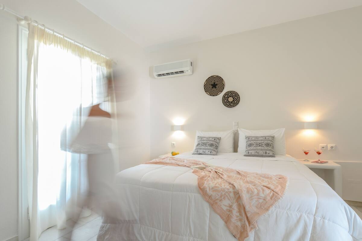 A bedroom with a bed, bedside tables, an air conditioner, and decorative wall art.