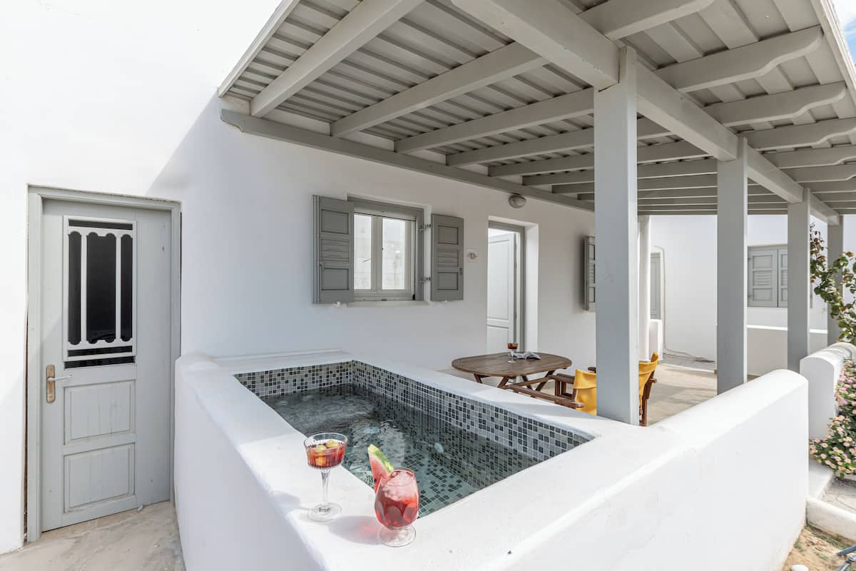 A white outdoor hot tub with two drinks, a wooden table, and a covered patio area.