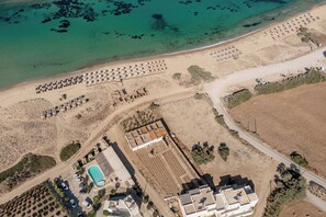 An aerial view of a coastal property with a beach, a swimming pool, and several buildings. - Golden Sand Naxos (Naxos)